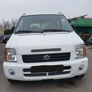 Suzuki Wagon R+ blanc de face avec sa calandre noire, stationné près d'un conteneur vert Trouillet.