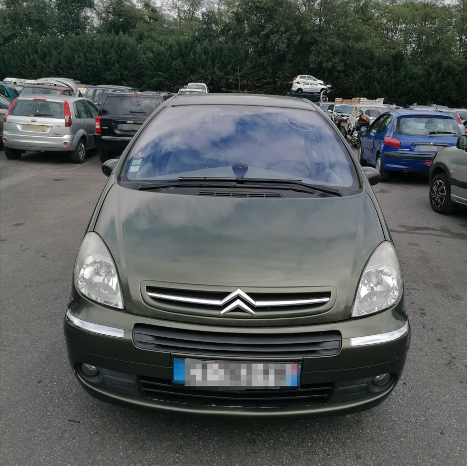 Citroën Xsara Picasso vert olive stationnée dans une casse automobile entourée d'autres véhicules d'occasion.