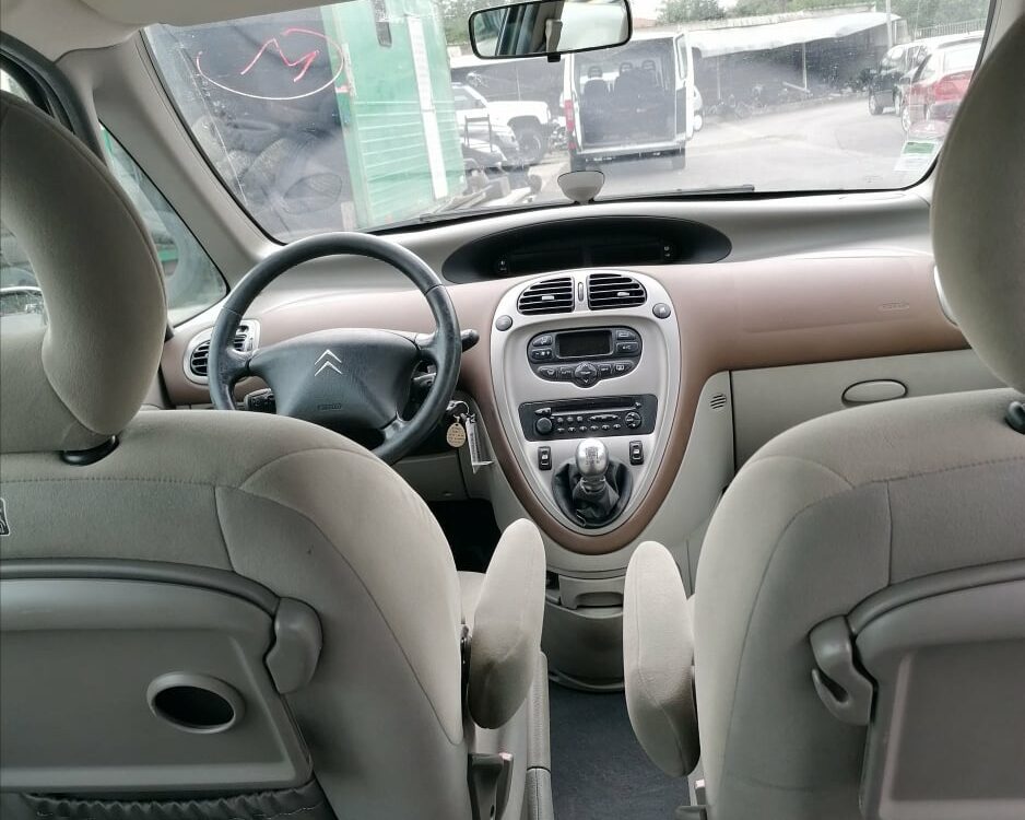 Intérieur d'une Citroën Xsara Picasso avec sièges en tissu gris et tableau de bord central numérique.