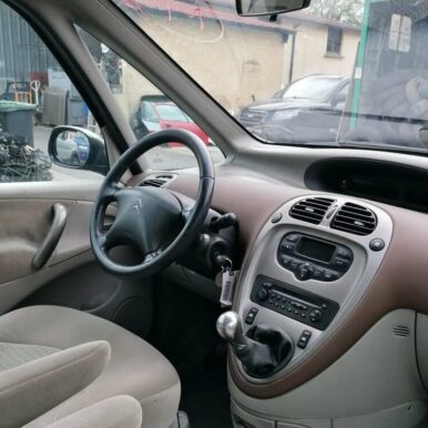 Intérieur d'une Citroën Xsara Picasso avec volant, tableau de bord central et levier de vitesse dans un garage.