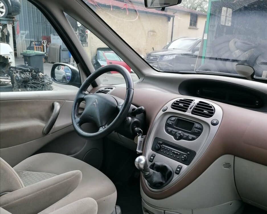 Intérieur d'une Citroën Xsara Picasso avec volant, tableau de bord central et levier de vitesse dans un garage.