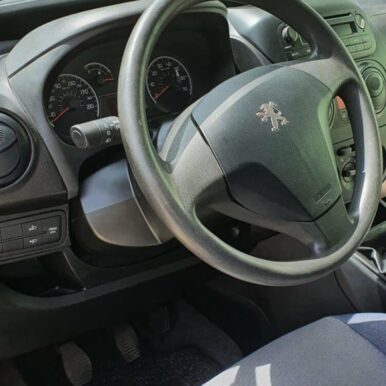 Tableau de bord de voiture Peugeot avec volant noir, compteur de vitesse et levier de vitesses manuel.