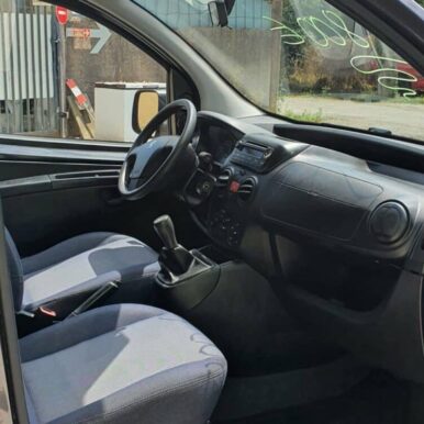 Intérieur d'un utilitaire Peugeot avec sièges en tissu gris, tableau de bord noir, volant et levier de vitesse manuel.